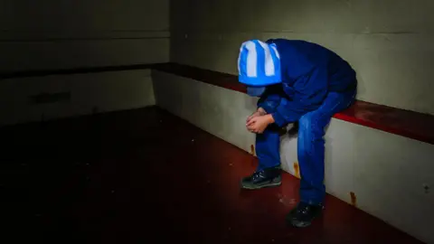 Stock photo of a boy wearing hood and blue jeans bent over with face hidden in a police cell