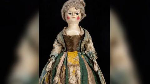 An antique doll wearing a green and gold dress