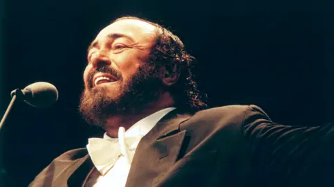 Getty Images Pavarotti, dressed in distinctive opera jacket and white bow tie, singing into a microphone