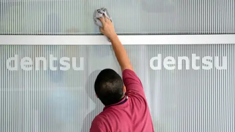 Getty Images This picture taken on July 14, 2012, shows a man cleaning a window at an entrance of the headquarters of Japan's top advertising agency Dentsu