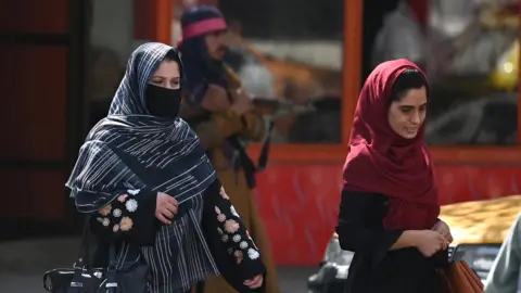 AAMIR QURESHI Afghan women walk past a Taliban fighter in a Kabul street