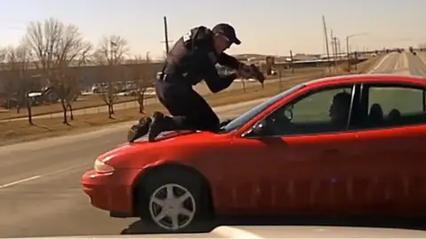 Officer on car bonnet pointing gun at passenger