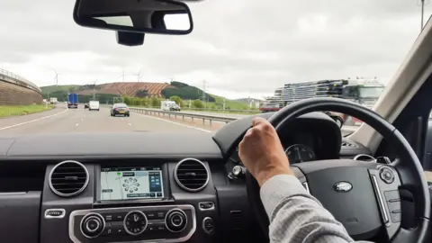 Getty Images A view from a Land Rover Discovery of a man driving on the M74 motorway, approaching the Clyde Wind Farm, with light traffic on the road.