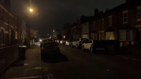 Cars parked either side of Arden Street in Earlsdon at night. A street light is on and shines across the pavement on either side with rows of terraced houses alongside.