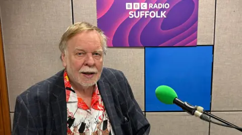 Rick Wakeman sitting at a piano in the BBC Radio Suffolk studio looking into the camera