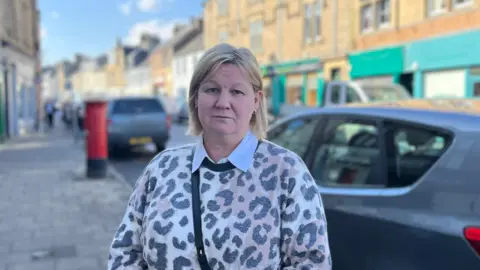 Women blonde and tata buthan animals facing the camera with a road scene behind him