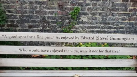 OpenBenches Bench dedication that says: “A good spot for a fine pint.” As enjoyed by Edward (Steve) Gunningham. Who would have enjoyed the view, were it not for that tree!