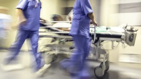 Getty Images A patient on a trolley wheeled by two nurses