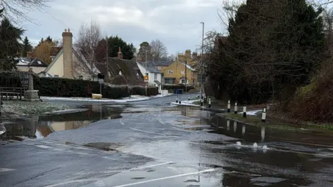 Picture of the street. Water can be seen flowing out onto the ground with cottages in the background.