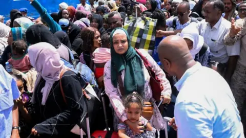 AFP via Getty Images People fleeing war-torn Sudan queue to board a boat from Port Sudan on April 28, 2023