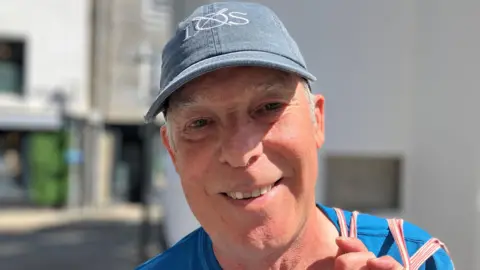A man wearing a baseball cap and smiling at the camera