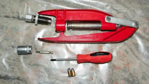 National Crime Agency A red, metal tool used to making bullets with. Next to it is a red screwdriver and a couple of gold bullets. 