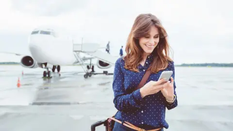 Getty Images Woman using smartphone in front of aeroplane