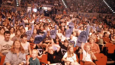 ITV/Shutterstock The crowd at the National Indoor Arena in Birmingham with many holding aloft "foam fingers"