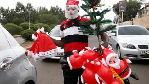 Getty Images A street vendor wearing a plastic Santa Claus mask peddles Christmas merchandise to motorists in Nairobi, Kenya.