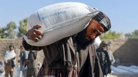 Getty Images Afghan people carry sacks of food grains distributed as an aid by the World Food Programme (WFP) in Kandahar on October 19, 2021