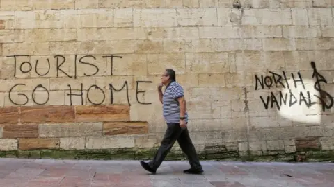 EPA A man walks past a "Tourists Go Home" graffitti on a wall close to the City Hall in Oviedo, northern Spain,