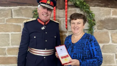 Carole Zambonini Carole Zambonini receiving her MBE from the Lord Lieutenant of Warwickshire Tim Cox