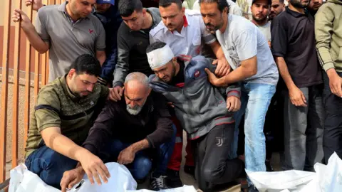 Palestinian men mourn beside the bodies of relatives killed in Israeli air strikes, at Nasser hospital, in Khan Younis, southern Gaza (15 May 2025)