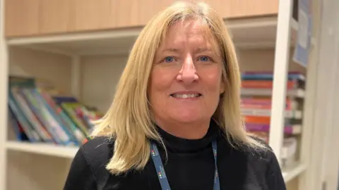 Debra Hennessy smiling at the camera wearing a black high-neck top. She is wearing a blue lanyard