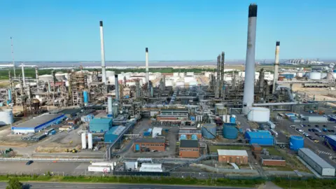 A drone view of the Prax Lindsey Oil Refinery. A cluster of metal structures rising to the blue sky.