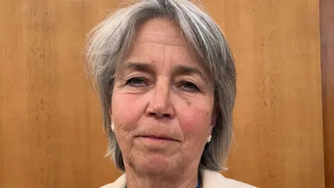 Councillor Elizabeth Threlfall with white earrings, mid length grey hair, looking at the camera with a slight smile. 