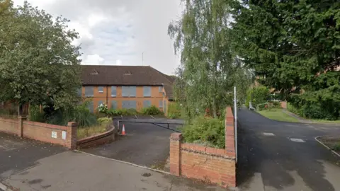 Boarded up apartments. The entry to a retirement estate can be seen next to an alleyway. It is overgrown. It looks abandoned. 