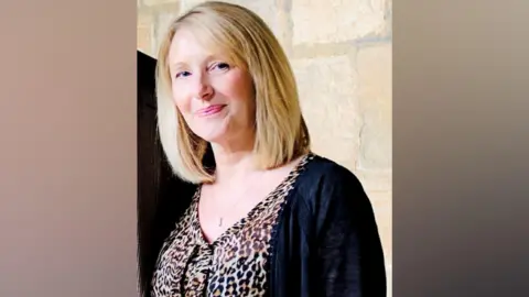 Lynne Hodgson has short straight blonde hair and blue eyes. She is wearing a leopard print top and a black cardigan.
