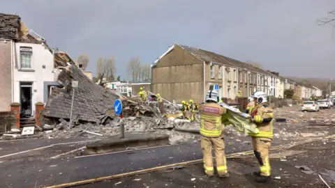 Pam Evans/PA Emergency workers are stood amidst the rubble of the collapsed house. The upper floor of the house is exposed and leaning down to the ground while officers remove rubble.