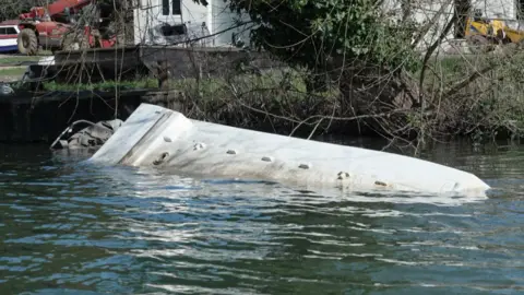 A upside down boat in the water that has clearly sunk.