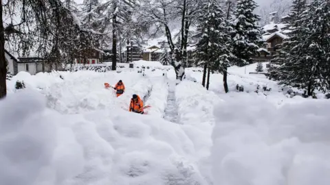 EPA Two workers in fluorescent orange remove the snow off a path in Zermatt - it is easily up to their waist in places as they shovel it aside