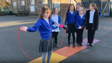 Zoey in a playground preparing to skip, with friends in the background encouraging her