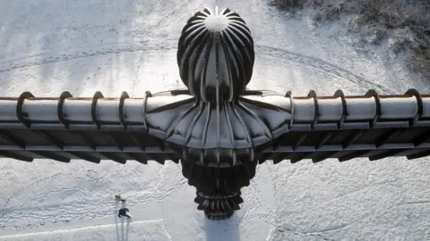 Owen Humphreys/PA Wire An aerial shot of The Angel of the North statue in Gateshead covered in snow, with walkers near its base