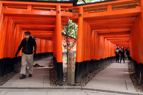 Getty Images A construction man wears a face mask while walking through the empty Torii gates of Fushimi Inari Taisha Shrine that are usually overrun by tourists on March 06, 2020 in Kyoto, Japan