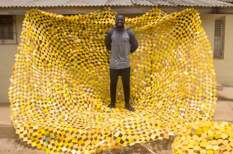 Nii Odzenma Serge Clottey standing on one of his tapestries in La - Accra, Ghana