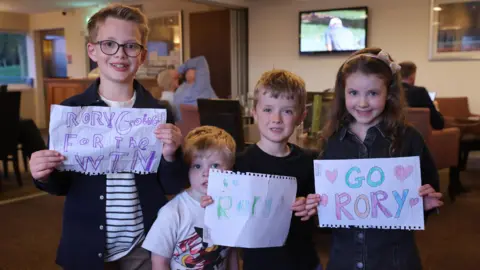 PA Media Four children smiling and holding paper notes showing support for Rory McIlroy.