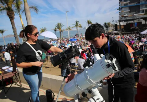 Henry Romero/Reuters A youngster and a woman prepare their telescopes as people gather and wait to observe a total solar eclipse in Mazatlan, Mexico April 8, 2024.