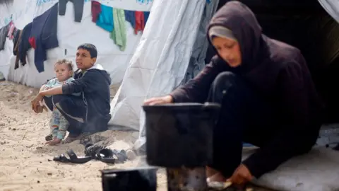 Reuters Displaced Palestinian children sit outside tents at a camp in Rafah, in the southern Gaza Strip (6 March 2024)