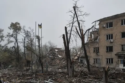 Getty Images Charred trees, a lone Ukrainian flag and the remains of a destroyed building in Avdiivka, Ukraine