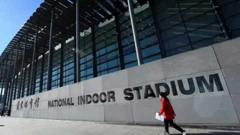 Getty Images A woman walks past the National Indoor Stadium before an ice hockey match, part of a 2022 Beijing Winter Olympic Games test event, in Beijing on November 10, 2021.