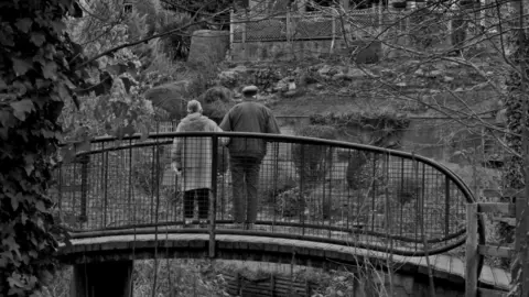 Lola Grey black and white image of two people on a bridge overlooking woodland