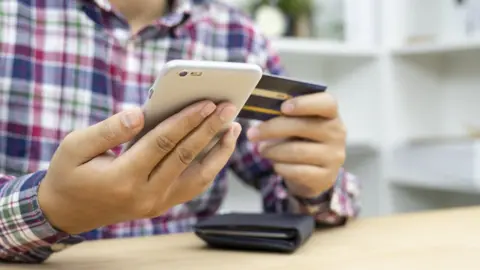 Getty Images Person with a smart phone and a bank card