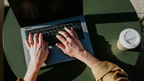 Getty Images A person using a laptop, with a cup of coffee next to them