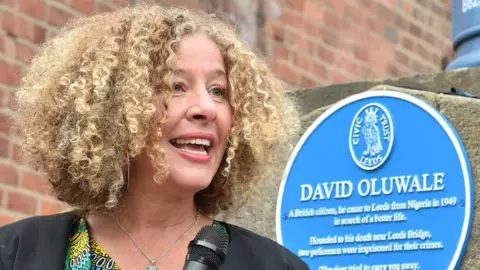 Emily Zobel Marshall Emily Zobel Marshall talking into a mic in front of the David Oluwale blue plaque
