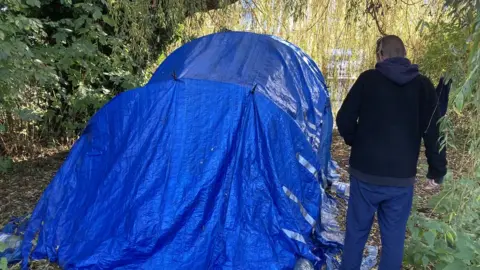 David Webster/BBC Man standing next to a tent