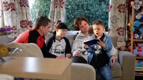 Jamie Niblock/BBC The famly around the table at their temporary home in Colchester