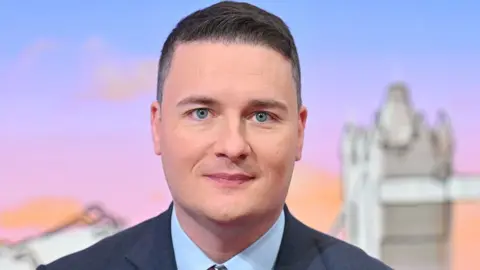 Head shot of Health Secretary Wes Streeting in a BBC studio. He is white, with short, dark hair and is wearing a dark blue suit and pale blue shirt