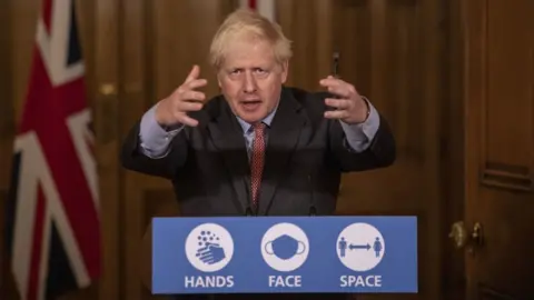 PA Media Boris Johnson speaks at the podium for a No 10 press office - it reads 'Hands. Face. Space'. He is gesturing with his arms up