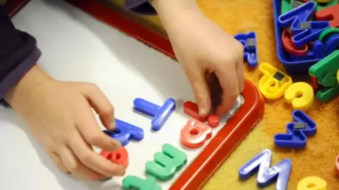 A primary school child at work in a classroom using magnetic letters on a white board