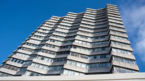 An 18-storey concrete tower block in a 1960s modernist style, as seen from below.